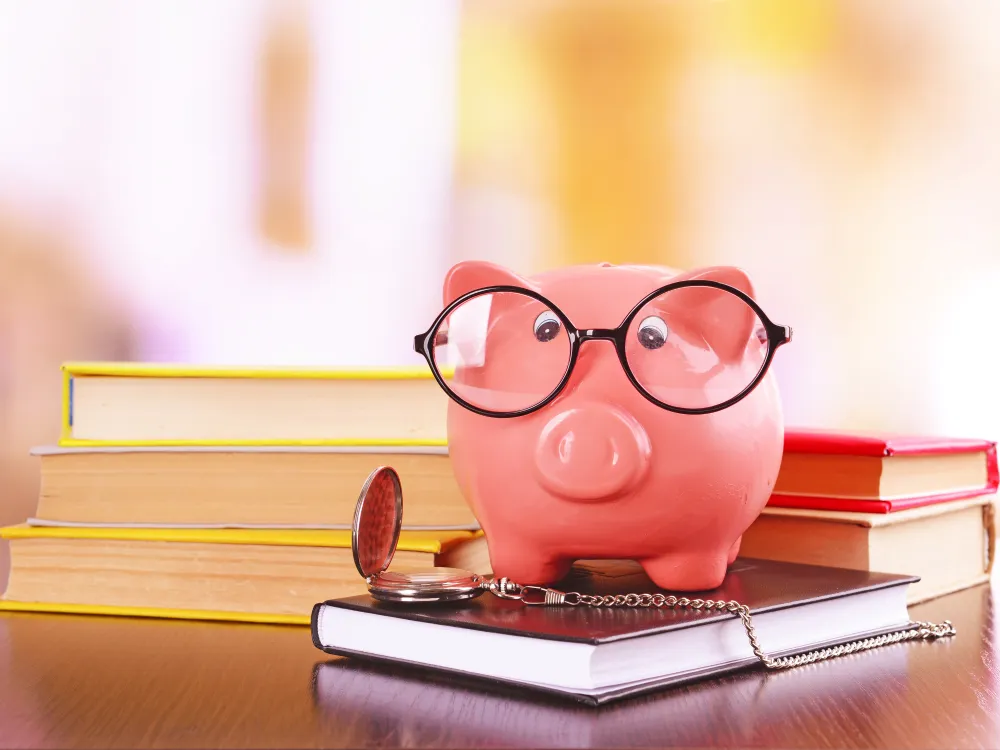 A cheerful pink piggy bank wearing glasses sits on books, symbolizing financial wisdom and education. A pocket watch rests nearby.