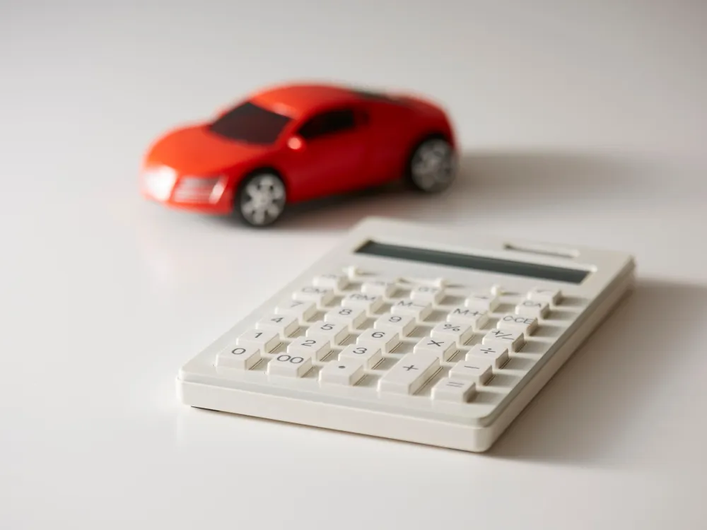 A white calculator with large buttons next to a bright red toy car, both placed on a clean, white surface.