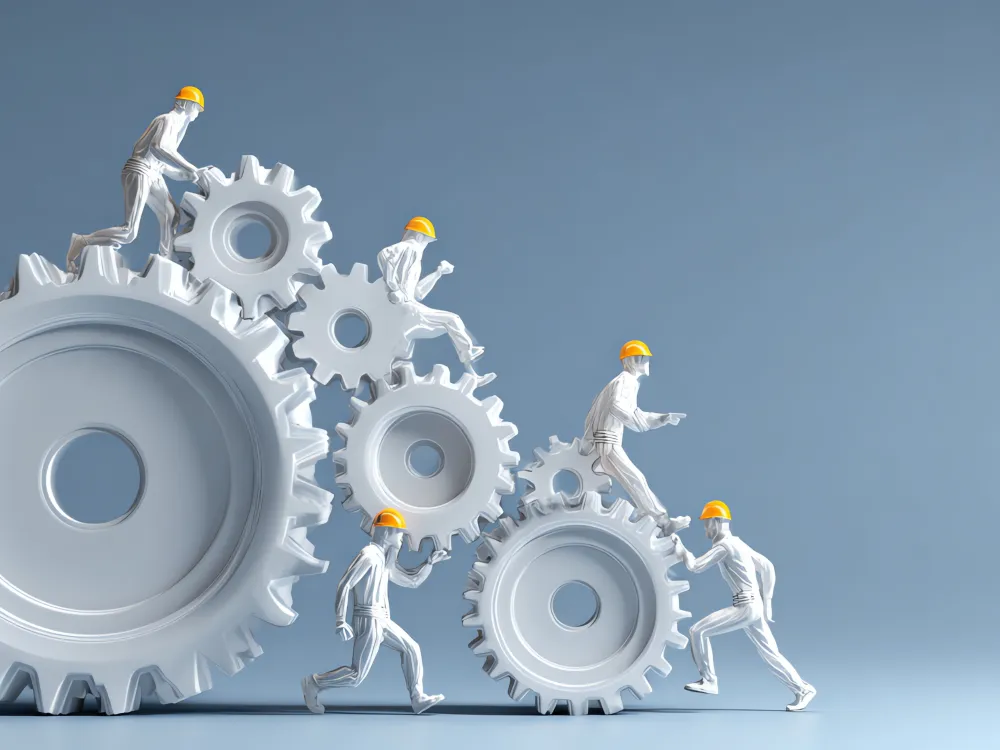 Five miniature workers in yellow hard hats climb and work on large white interlocking gears against a blue background.