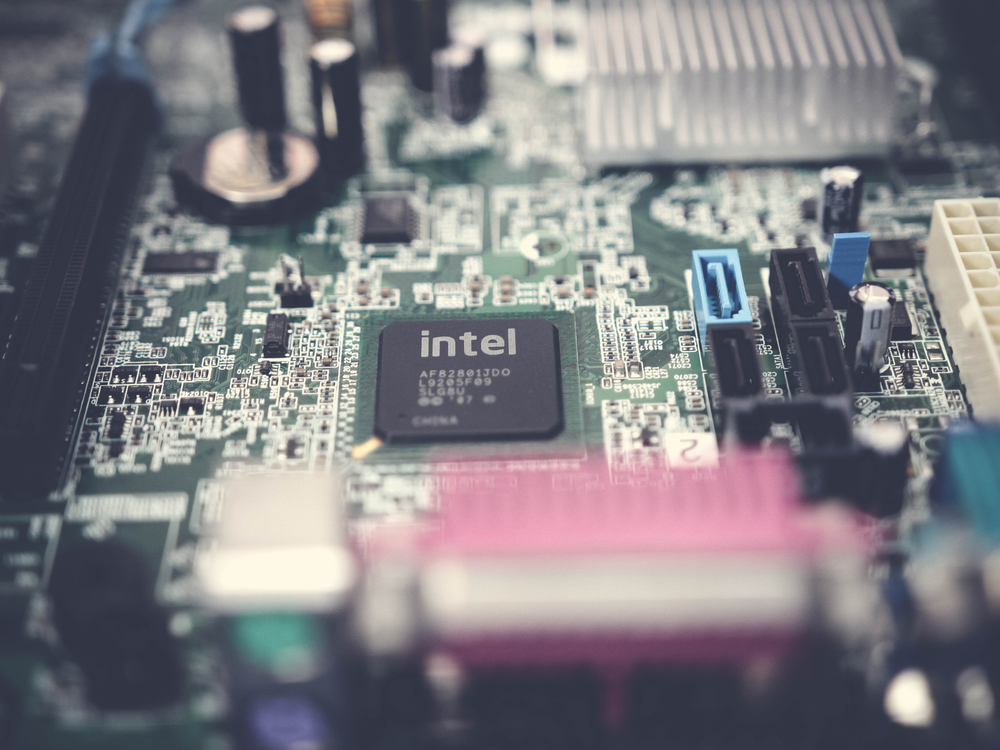 Close-up of a computer motherboard featuring an Intel processor, various capacitors, ports, and intricate circuitry details.