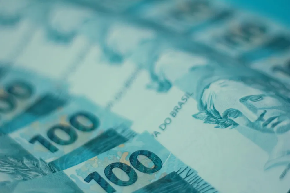 Close-up of several Brazilian 100 real banknotes, showing detailed blue design and partial faces on the currency.