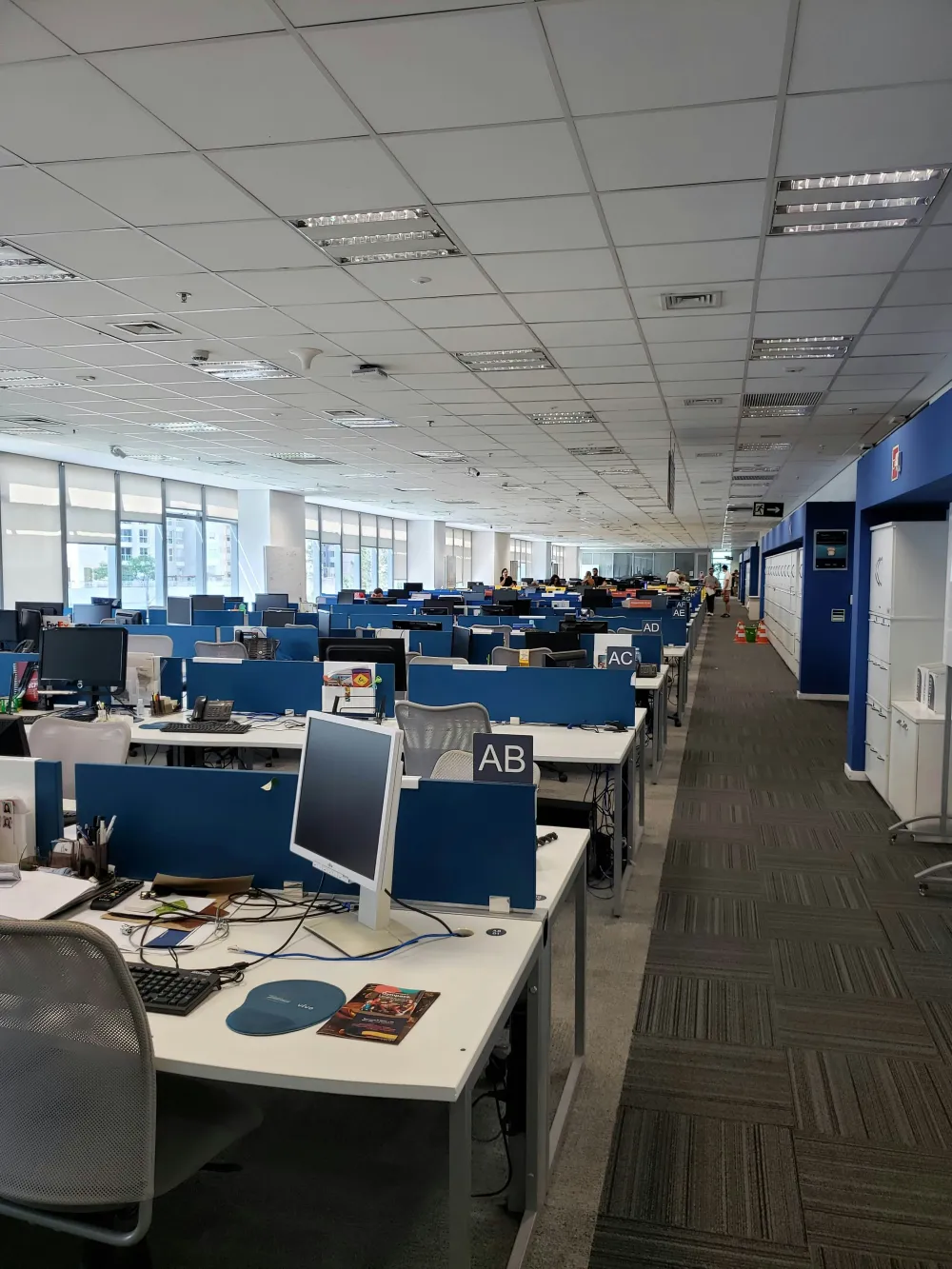 Open-plan office with rows of desks, computers, and employees working in a modern corporate workspace.