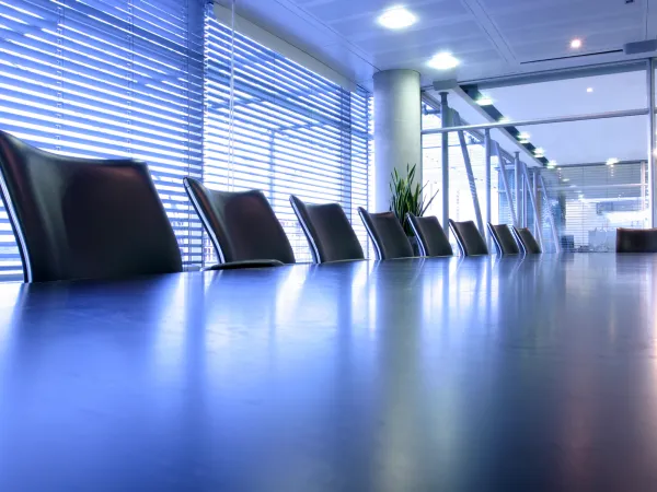 Modern conference room featuring a long table, black chairs, and large windows with blinds letting in natural light.