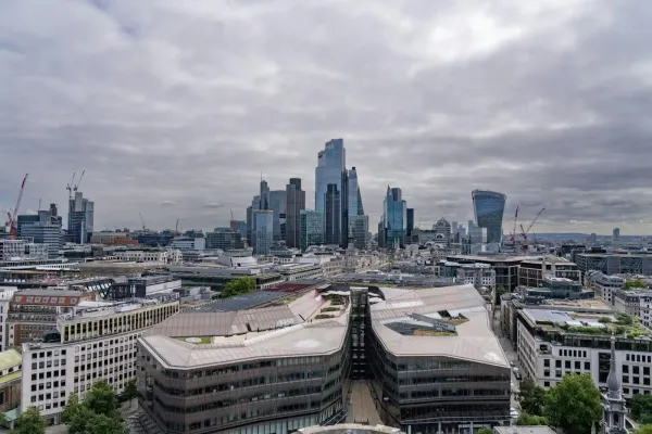 A panoramic view of London's skyline featuring modern skyscrapers, construction cranes, and a cloudy sky.